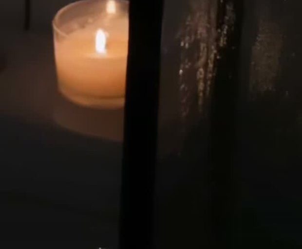 Vela acesa em um copo de vidro, em ambiente escuro