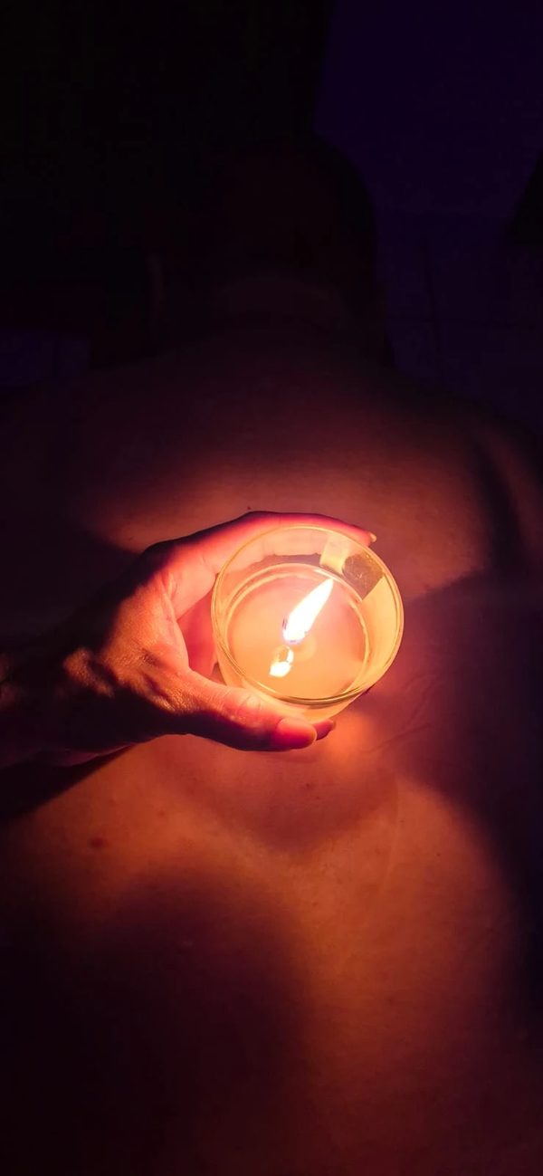 Mão de Lorena segurando uma vela acesa sobre as costas do cliente